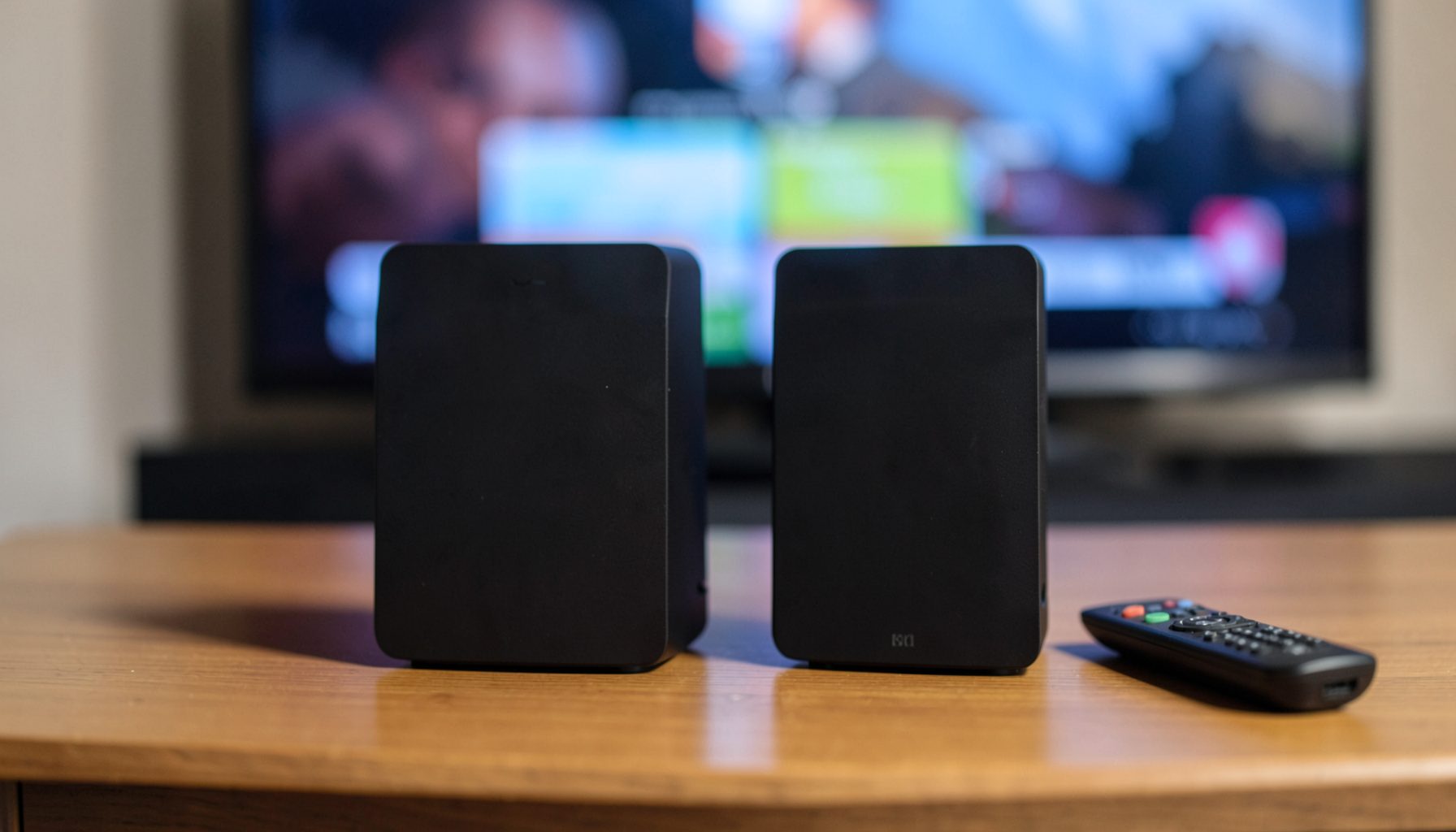Deux boîtiers TV Box noirs posés sur un meuble, télécommande à côté, écran de télévision flou en arrière-plan