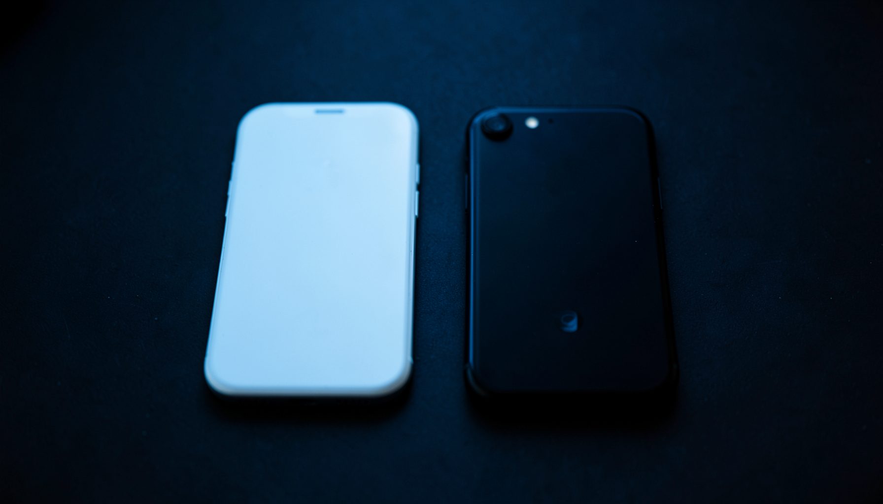 Deux smartphones côte à côte sur une surface sombre, l'un blanc l'autre noir, éclairage tamisé bleuté