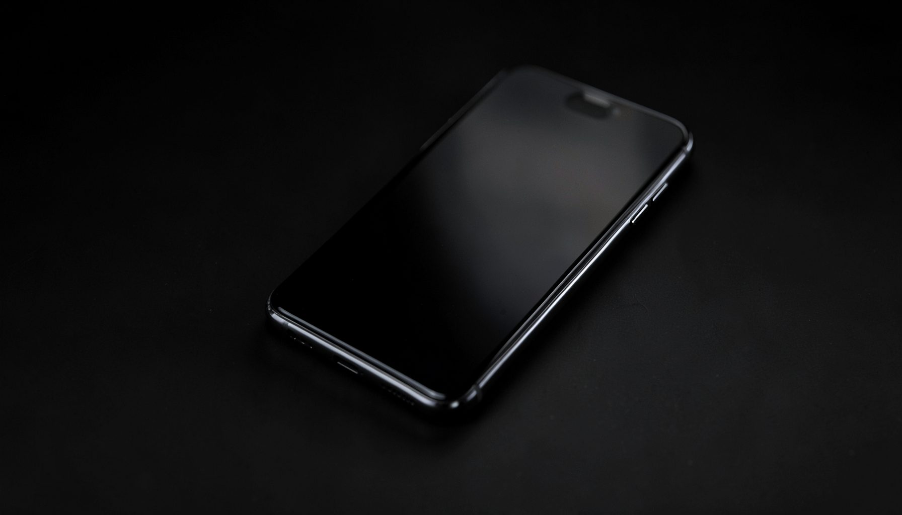 Smartphone noir brillant posé de trois-quarts sur fond sombre, reflets métalliques discrets